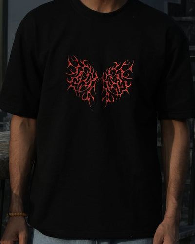 Person wearing a black t-shirt with red design and blue jeans standing on a reflective surface.